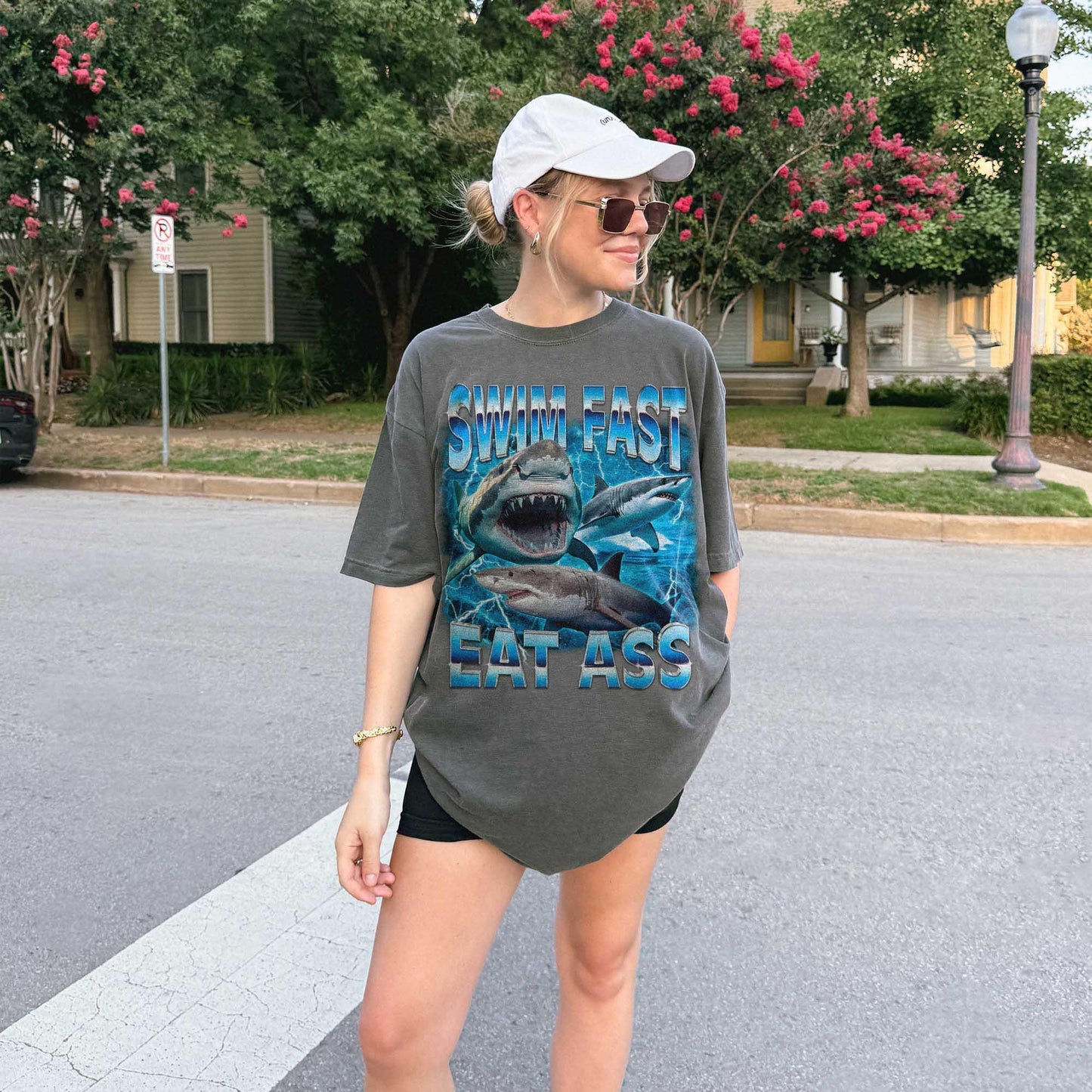 Funny adult humor graphic tee featuring three fierce sharks swimming aggressively with the edgy phrase "Swim Fast Eat Ass." Vibrant vintage-style design with bold blue letters and ocean wave graphics. Perfect meme culture shirt for young adults, shark lovers, sarcastic friends, or edgy trendsetters. Ideal casual tee for Shark Week, beach trips, parties, or humorous gifts. Provocative yet playful, this shirt makes a bold style statement.