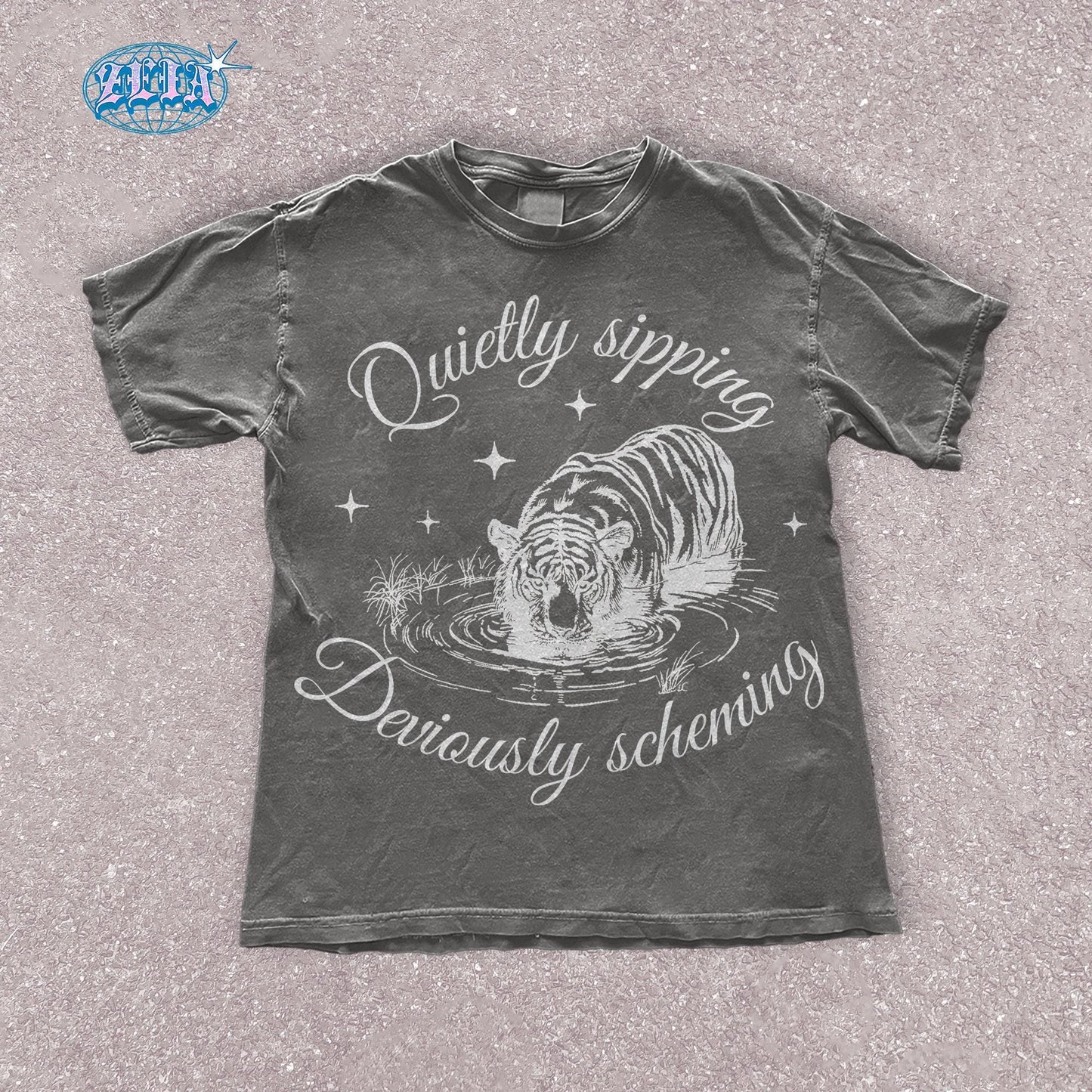 A pepper t-shirt featuring a detailed black graphic of a tiger quietly sipping water with the text Quietly sipping, deviously scheming elegantly curved above and below the tiger.