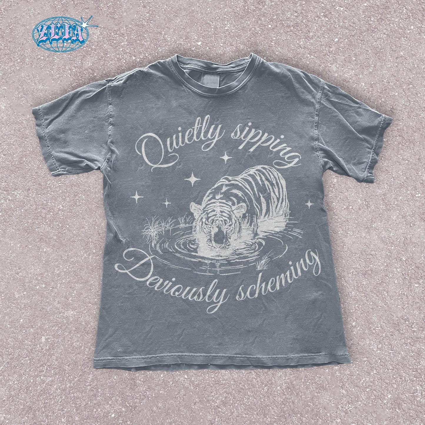A blue jean t-shirt featuring a detailed black graphic of a tiger quietly sipping water with the text Quietly sipping, deviously scheming elegantly curved above and below the tiger.