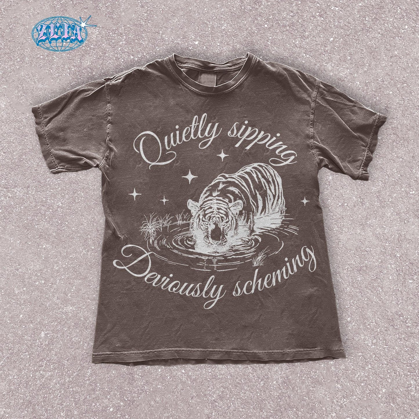A brown espresso t-shirt featuring a detailed black graphic of a tiger quietly sipping water with the text Quietly sipping, deviously scheming elegantly curved above and below the tiger.