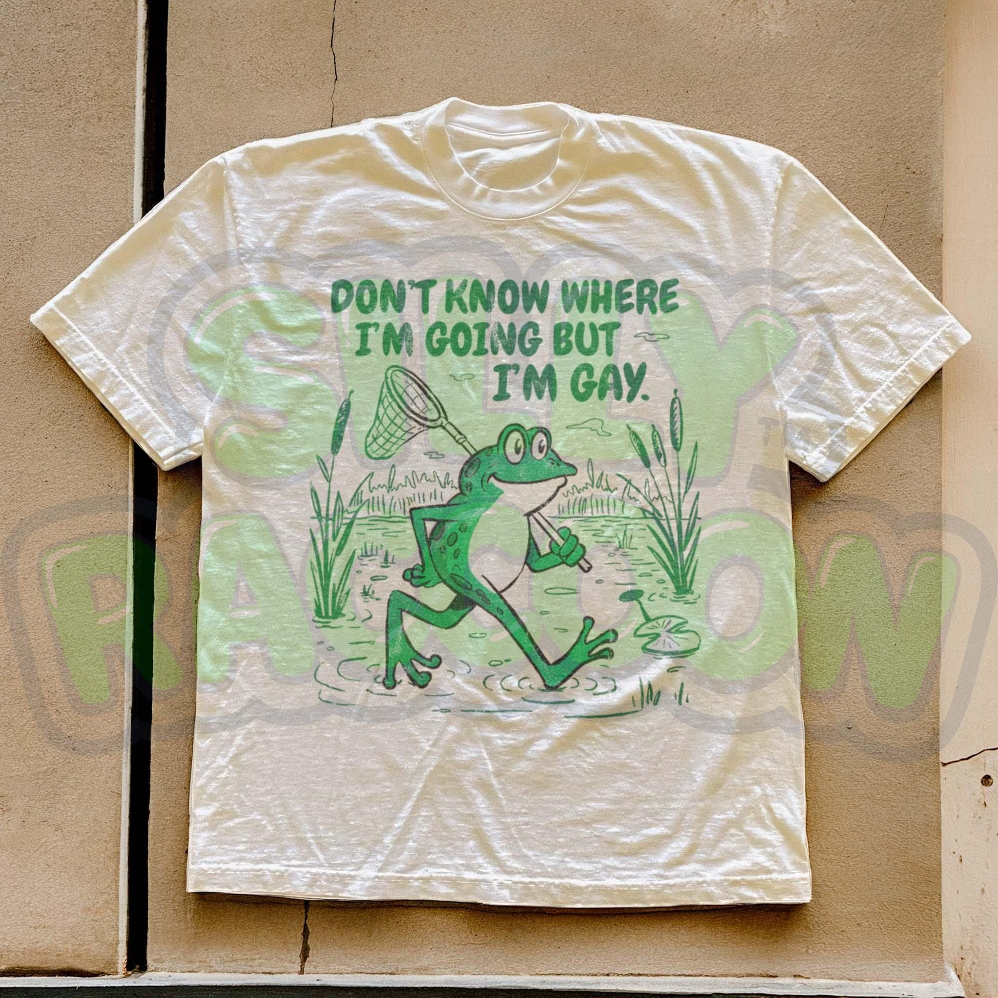 Funny Gay Frog Shirt for men and women featuring a green cartoon frog walking through a marsh carrying a butterfly net over its shoulder. Above the frog, the text reads &quot;DON&#39;T KNOW WHERE I&#39;M GOING BUT I&#39;M GAY&quot; in bold green font. The illustration has a vintage, slightly distressed graphic tee style. This unisex LGBTQ pride t-shirt is a humorous gift for gay friends, perfect for Pride Month or as a coming out gift.