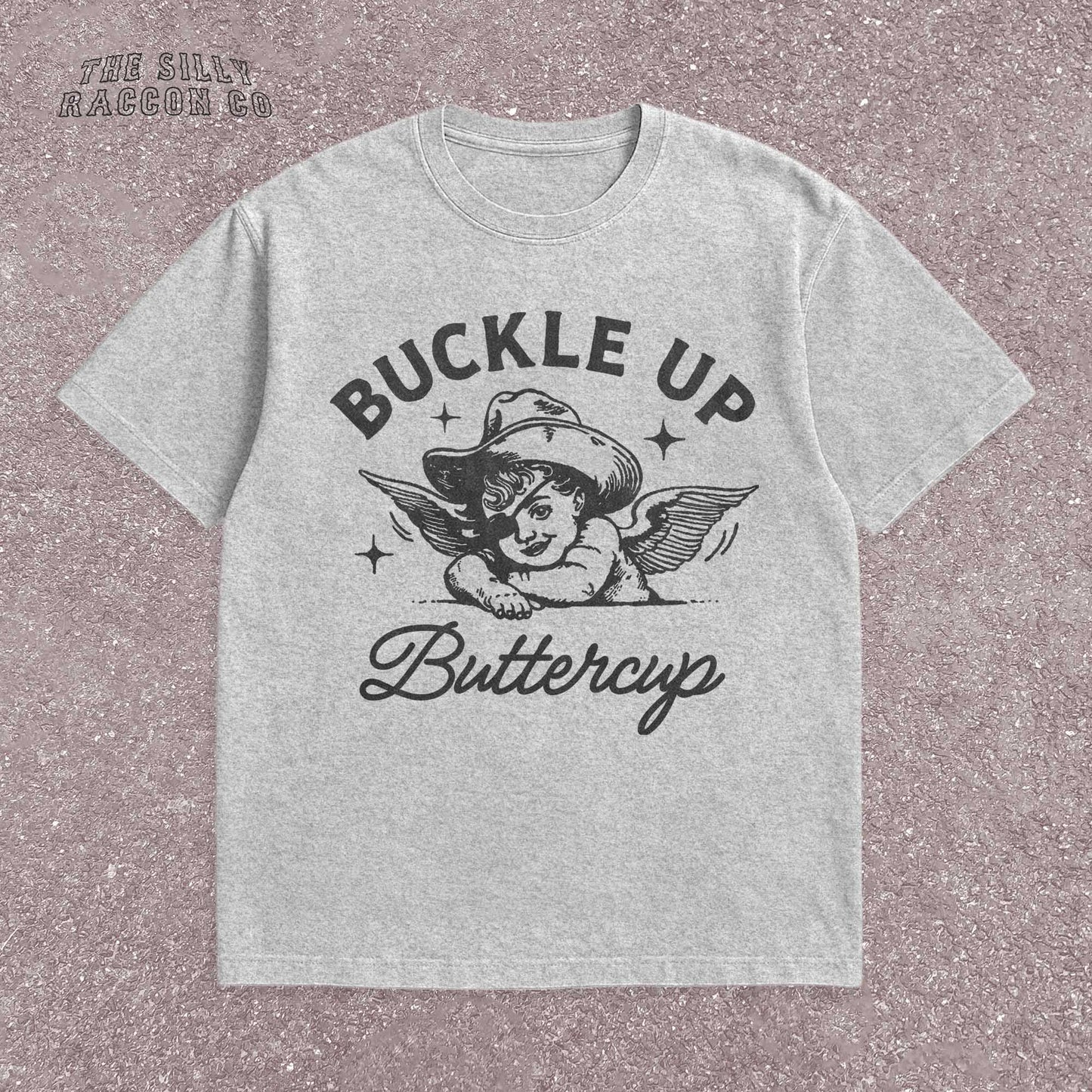 Funny western shirt for women featuring a vintage cowboy angel with wings and the quote &quot;Buckle Up Buttercup&quot; in bold retro typography. The design blends southern sass with angelcore and rodeo aesthetics, perfect for cowgirl fashion or western gifts. Great as a vintage graphic tee with humor and charm for her, ideal for gifting or personal style with a nostalgic Y2K vibe.