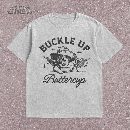 Funny western shirt for women featuring a vintage cowboy angel with wings and the quote &quot;Buckle Up Buttercup&quot; in bold retro typography. The design blends southern sass with angelcore and rodeo aesthetics, perfect for cowgirl fashion or western gifts. Great as a vintage graphic tee with humor and charm for her, ideal for gifting or personal style with a nostalgic Y2K vibe.
