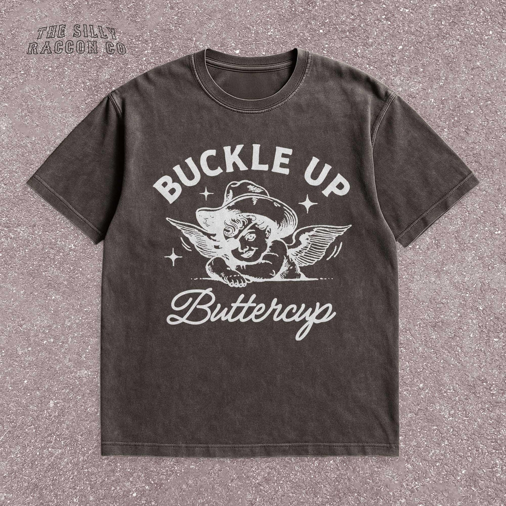 Funny western shirt for women featuring a vintage cowboy angel with wings and the quote &quot;Buckle Up Buttercup&quot; in bold retro typography. The design blends southern sass with angelcore and rodeo aesthetics, perfect for cowgirl fashion or western gifts. Great as a vintage graphic tee with humor and charm for her, ideal for gifting or personal style with a nostalgic Y2K vibe.