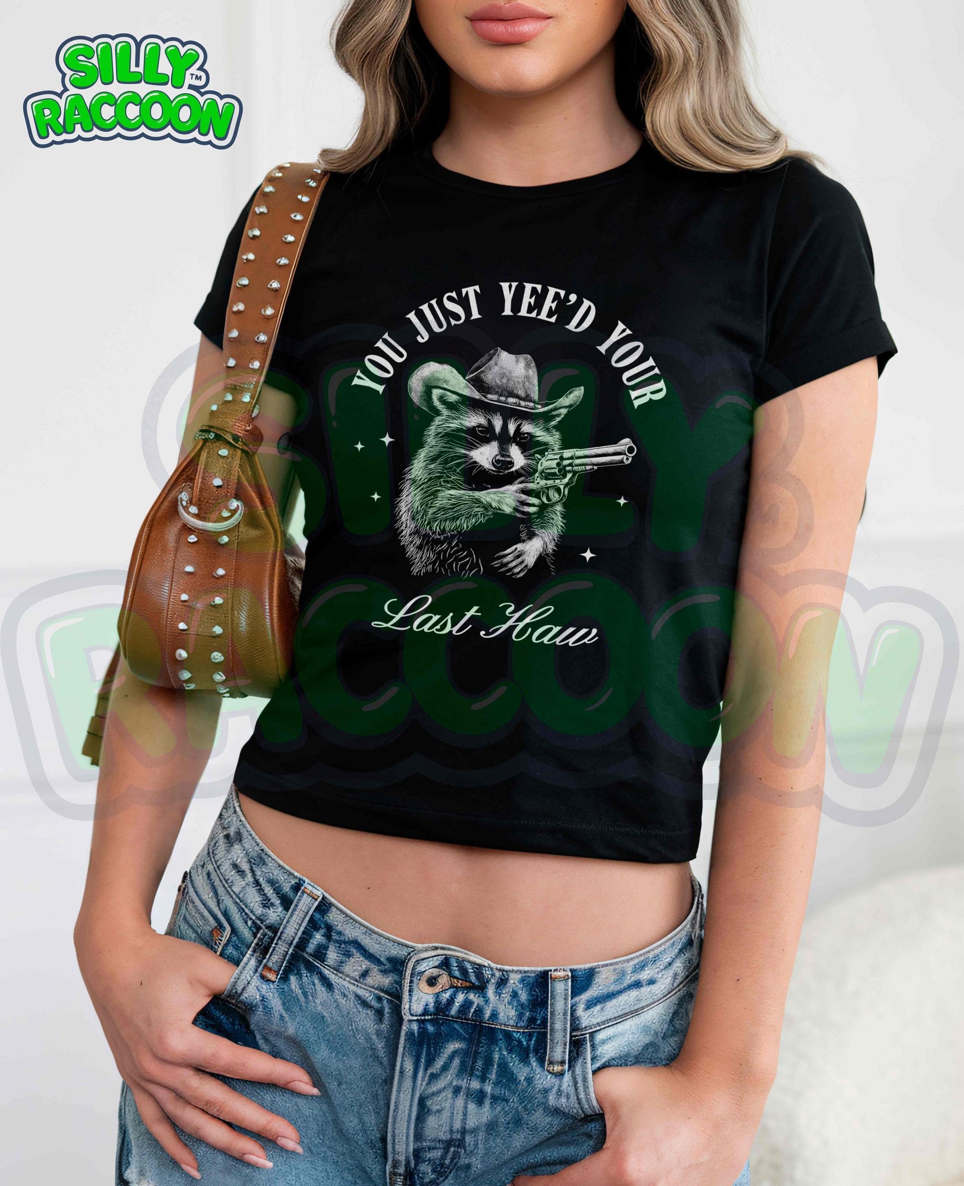 Funny western crop top for women featuring a detailed sketch of a raccoon wearing a cowboy hat and aiming a pistol. The text &quot;You Just Yee&#39;d Your Last Haw&quot; surrounds the raccoon graphic. This humorous graphic tee blends country and meme culture, perfect for young adults and women who love sarcastic animal shirts. Ideal gift for country girls, raccoon lovers, or anyone who enjoys funny southern sayings and western meme apparel.