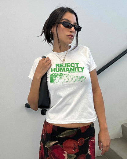 Young woman wearing a white Y2K baby tee, perfect for Gen Z fashion lovers and teens into alt clothing. The shirt features a green graphic print with the text &quot;REJECT HUMANITY RETURN TO FROG&quot; and an illustration showing human faces morphing into frogs. This funny meme shirt taps into internet culture and weirdcore aesthetic. It&#39;s a great sarcastic gift for anti-social friends or any frog lover. Ideal casual wear top, this graphic tee suits everyday outfits or alternative style look