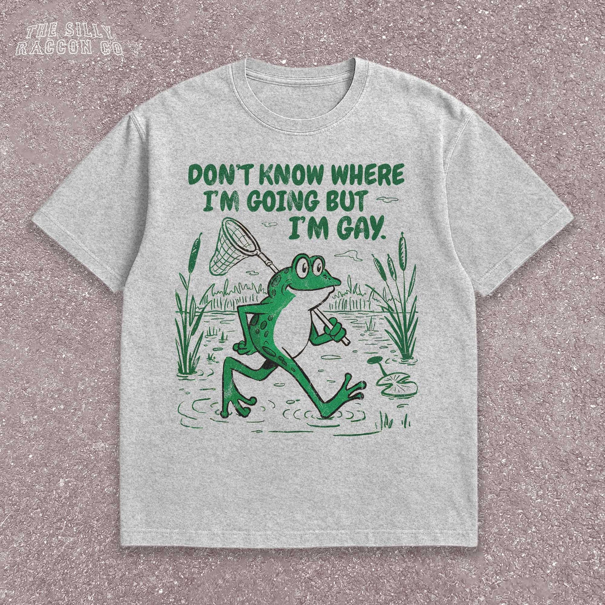 Funny Gay Frog Shirt for men and women featuring a green cartoon frog walking through a marsh carrying a butterfly net over its shoulder. Above the frog, the text reads &quot;DON&#39;T KNOW WHERE I&#39;M GOING BUT I&#39;M GAY&quot; in bold green font. The illustration has a vintage, slightly distressed graphic tee style. This unisex LGBTQ pride t-shirt is a humorous gift for gay friends, perfect for Pride Month or as a coming out gift.