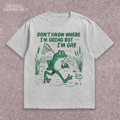 Funny Gay Frog Shirt for men and women featuring a green cartoon frog walking through a marsh carrying a butterfly net over its shoulder. Above the frog, the text reads &quot;DON&#39;T KNOW WHERE I&#39;M GOING BUT I&#39;M GAY&quot; in bold green font. The illustration has a vintage, slightly distressed graphic tee style. This unisex LGBTQ pride t-shirt is a humorous gift for gay friends, perfect for Pride Month or as a coming out gift.