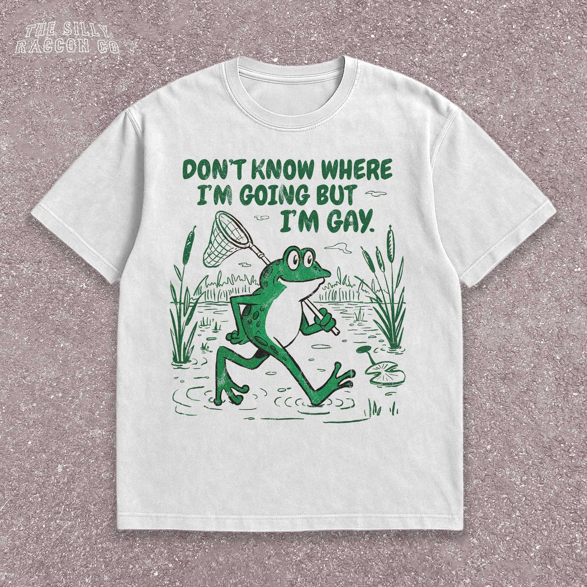 Funny Gay Frog Shirt for men and women featuring a green cartoon frog walking through a marsh carrying a butterfly net over its shoulder. Above the frog, the text reads &quot;DON&#39;T KNOW WHERE I&#39;M GOING BUT I&#39;M GAY&quot; in bold green font. The illustration has a vintage, slightly distressed graphic tee style. This unisex LGBTQ pride t-shirt is a humorous gift for gay friends, perfect for Pride Month or as a coming out gift.