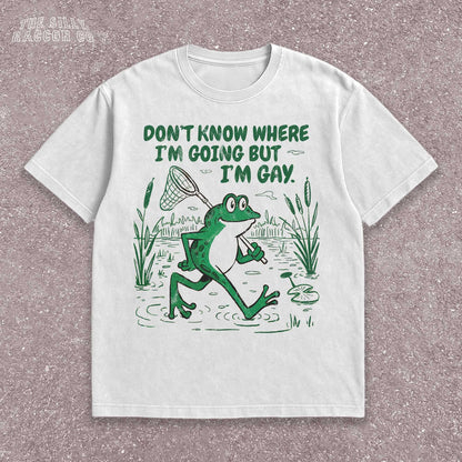 Funny Gay Frog Shirt for men and women featuring a green cartoon frog walking through a marsh carrying a butterfly net over its shoulder. Above the frog, the text reads &quot;DON&#39;T KNOW WHERE I&#39;M GOING BUT I&#39;M GAY&quot; in bold green font. The illustration has a vintage, slightly distressed graphic tee style. This unisex LGBTQ pride t-shirt is a humorous gift for gay friends, perfect for Pride Month or as a coming out gift.