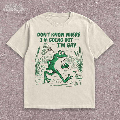 Funny Gay Frog Shirt for men and women featuring a green cartoon frog walking through a marsh carrying a butterfly net over its shoulder. Above the frog, the text reads &quot;DON&#39;T KNOW WHERE I&#39;M GOING BUT I&#39;M GAY&quot; in bold green font. The illustration has a vintage, slightly distressed graphic tee style. This unisex LGBTQ pride t-shirt is a humorous gift for gay friends, perfect for Pride Month or as a coming out gift.