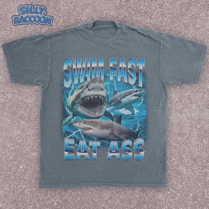 Funny adult humor graphic tee featuring three fierce sharks swimming aggressively with the edgy phrase &quot;Swim Fast Eat Ass.&quot; Vibrant vintage-style design with bold blue letters and ocean wave graphics. Perfect meme culture shirt for young adults, shark lovers, sarcastic friends, or edgy trendsetters. Ideal casual tee for Shark Week, beach trips, parties, or humorous gifts. Provocative yet playful, this shirt makes a bold style statement.