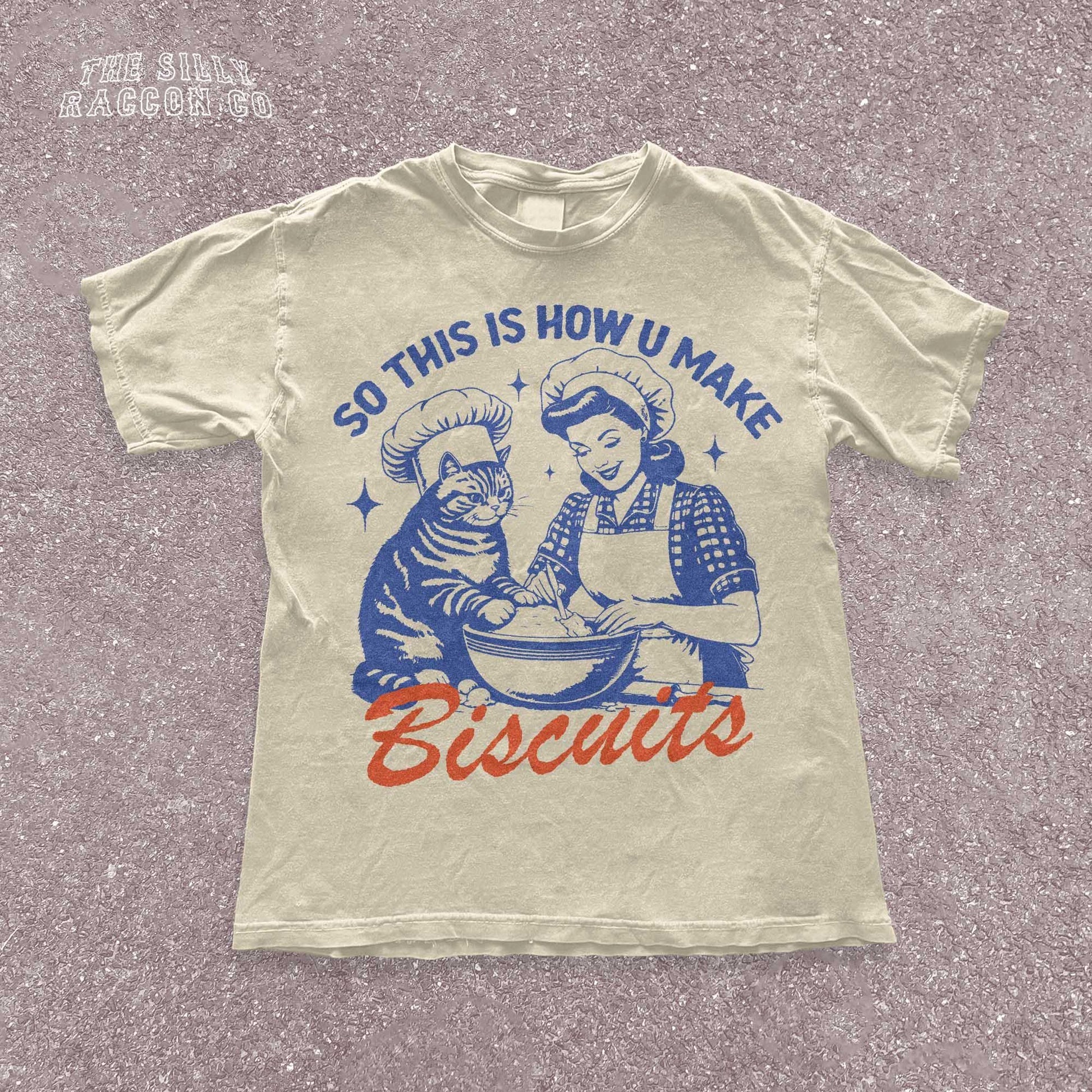 Funny cat t-shirt for men and women featuring a vintage-style illustration of a woman and a cat &quot;making biscuits&quot; together in a mixing bowl. The cat wears a chef hat, humorously mimicking the kneading behavior cats are known for. Retro colors and design give it a nostalgic feel. Great for cat lovers, pet parents, and fans of funny animal shirts. Makes a perfect gift for cat moms, dads, or kitchen humor enthusiasts.