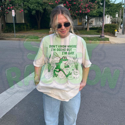 Funny Gay Frog Shirt for men and women featuring a green cartoon frog walking through a marsh carrying a butterfly net over its shoulder. Above the frog, the text reads &quot;DON&#39;T KNOW WHERE I&#39;M GOING BUT I&#39;M GAY&quot; in bold green font. The illustration has a vintage, slightly distressed graphic tee style. This unisex LGBTQ pride t-shirt is a humorous gift for gay friends, perfect for Pride Month or as a coming out gift.
