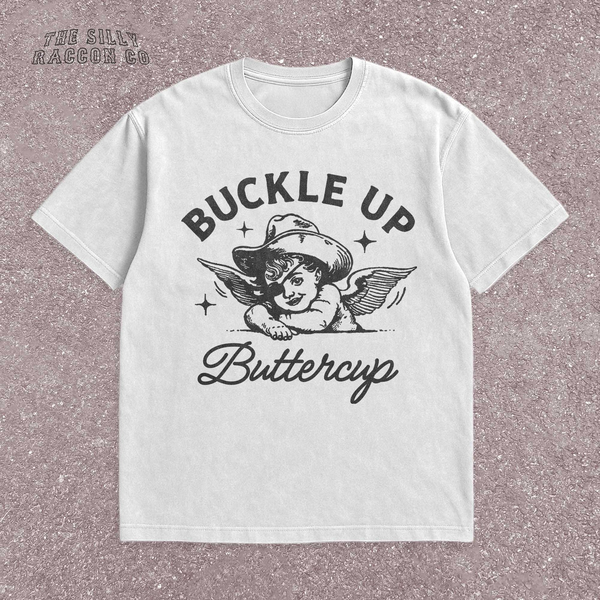 Funny western shirt for women featuring a vintage cowboy angel with wings and the quote &quot;Buckle Up Buttercup&quot; in bold retro typography. The design blends southern sass with angelcore and rodeo aesthetics, perfect for cowgirl fashion or western gifts. Great as a vintage graphic tee with humor and charm for her, ideal for gifting or personal style with a nostalgic Y2K vibe.