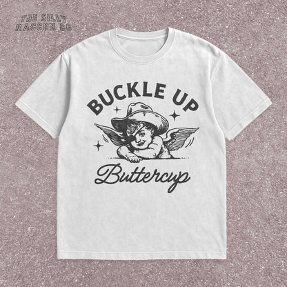 Funny western shirt for women featuring a vintage cowboy angel with wings and the quote &quot;Buckle Up Buttercup&quot; in bold retro typography. The design blends southern sass with angelcore and rodeo aesthetics, perfect for cowgirl fashion or western gifts. Great as a vintage graphic tee with humor and charm for her, ideal for gifting or personal style with a nostalgic Y2K vibe.