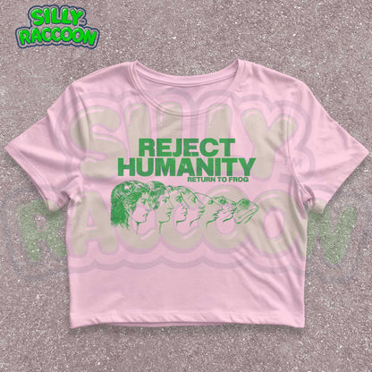 Young woman wearing a white Y2K baby tee, perfect for Gen Z fashion lovers and teens into alt clothing. The shirt features a green graphic print with the text &quot;REJECT HUMANITY RETURN TO FROG&quot; and an illustration showing human faces morphing into frogs. This funny meme shirt taps into internet culture and weirdcore aesthetic. It&#39;s a great sarcastic gift for anti-social friends or any frog lover. Ideal casual wear top, this graphic tee suits everyday outfits or alternative style look